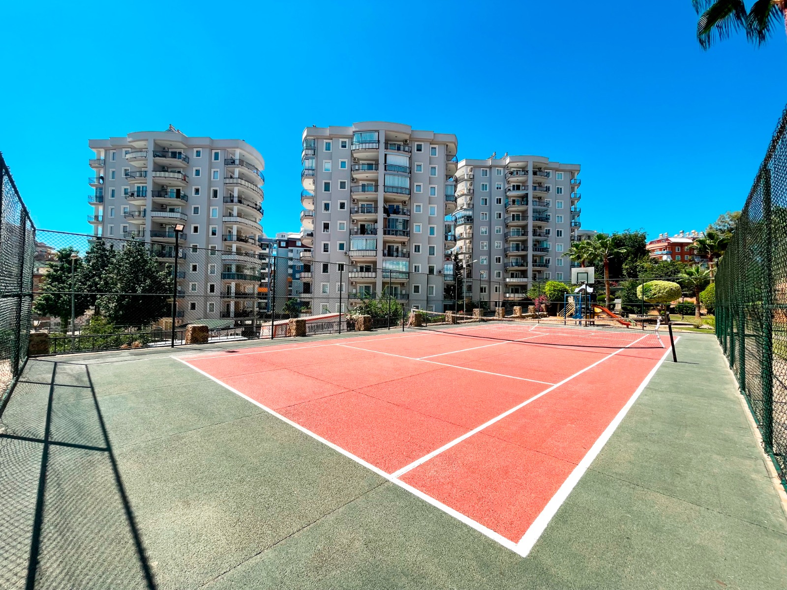 Kırmızı kort, tenis ağı ve basketbol potası bulunan spor alanı, daire sakinleri için