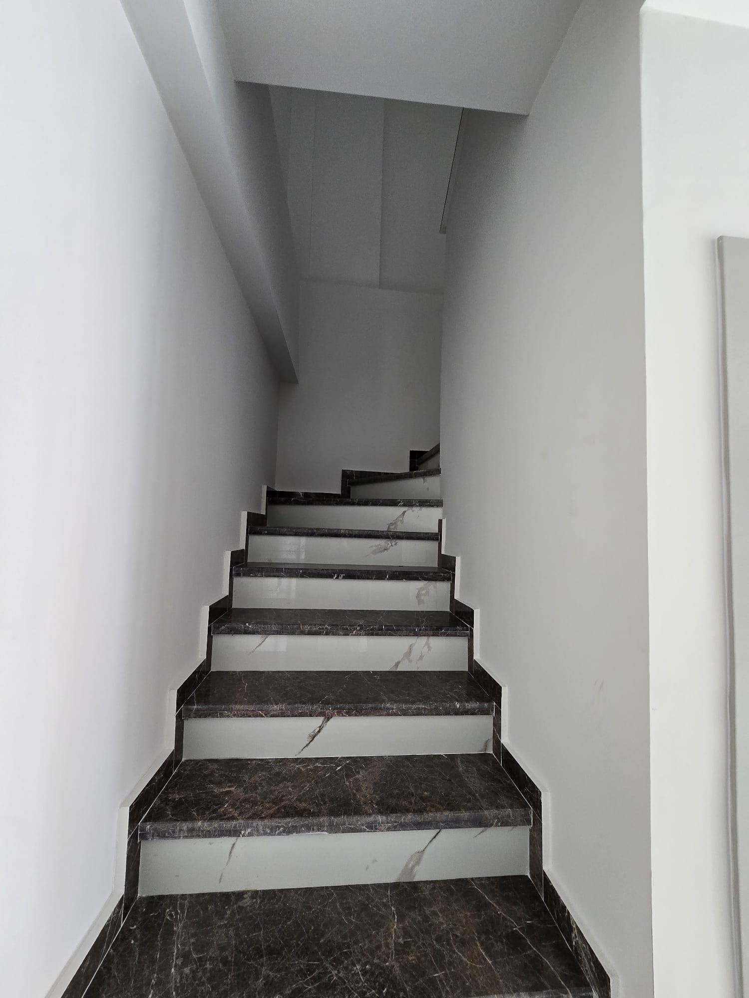 İç merdivende koyu mermer kaplama, beyaz desenli rıhtlar ve alçak tavanlı konut