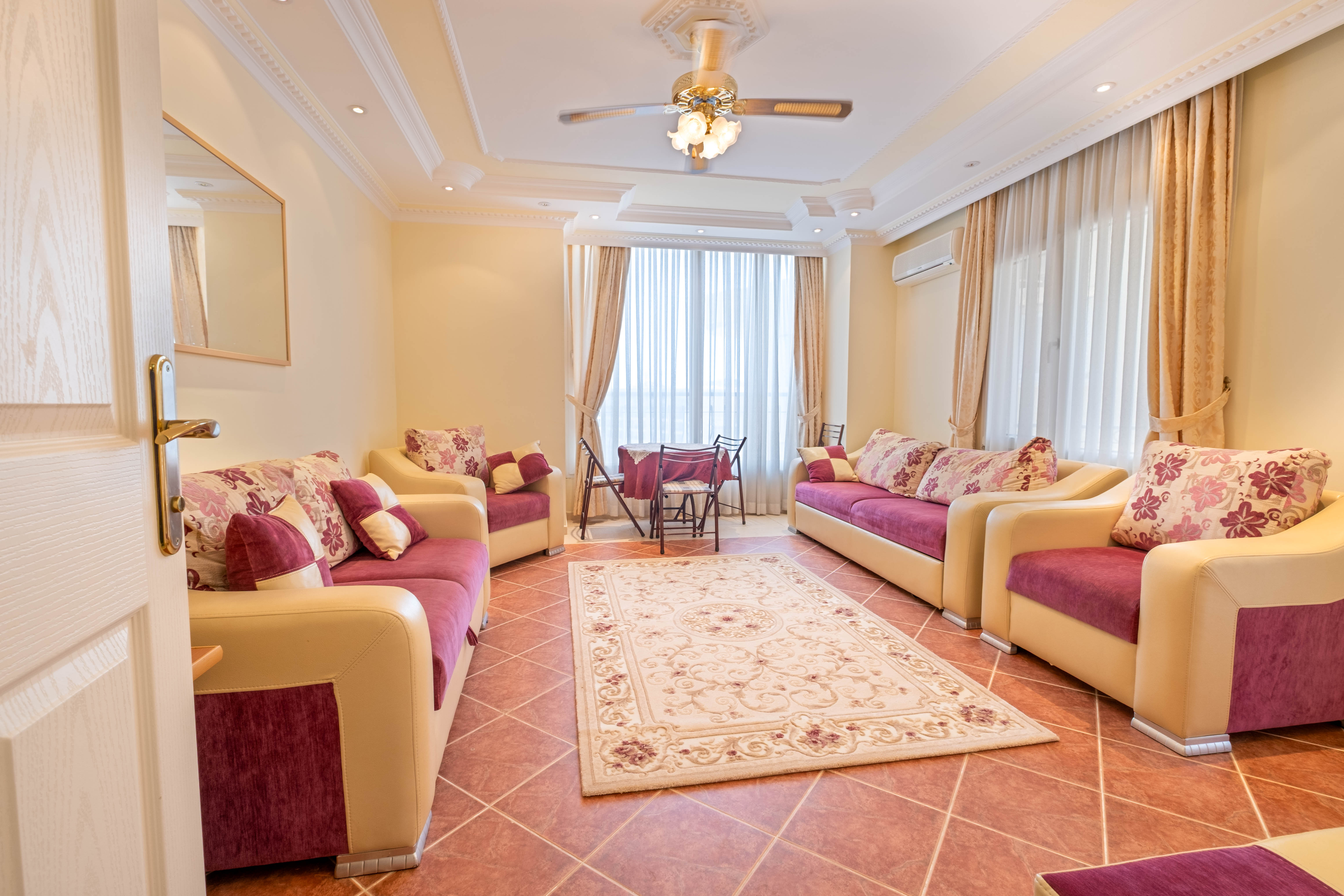 Tosmur’daki salon çiçek desenli kanepeler yuvarlak yemek masası ve panoramik pencereyle düzenlenmiş