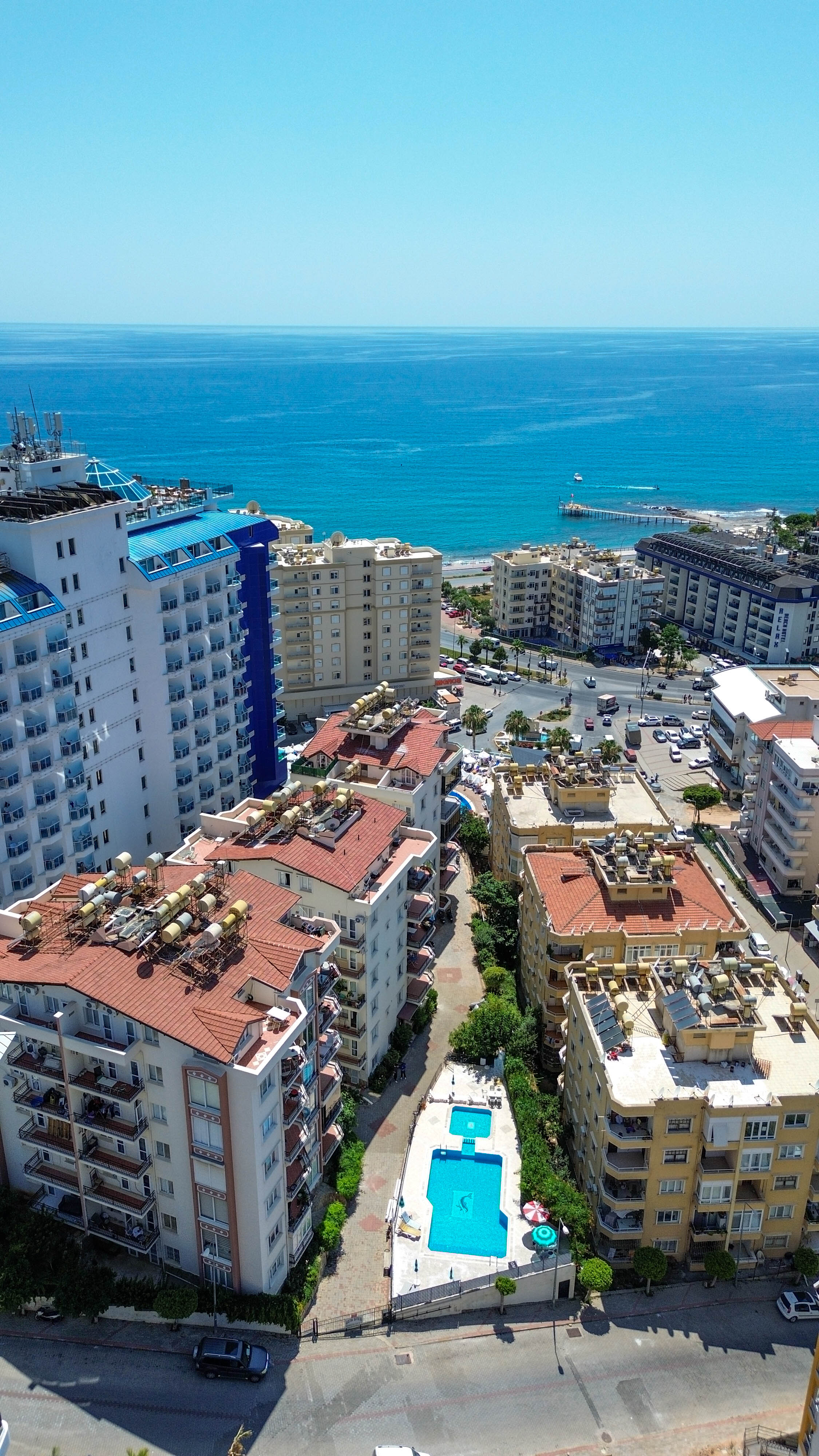 Kırmızı kiremit çatılar ve deniz panoraması Tosmur’daki rezidansların bulunduğu sitede avlu havuzunun üzerinde uzanıyor