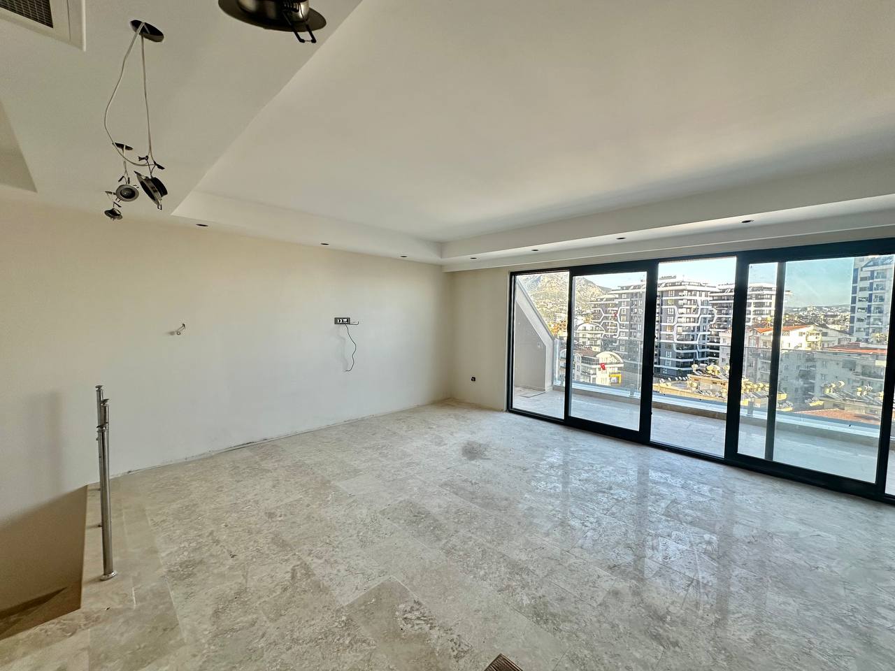 Sürgülü panoramik pencereli salon, Türkiye’de satılık penthouse içinde şehir ve dağ yamacı manzarasıyla uzanıyor