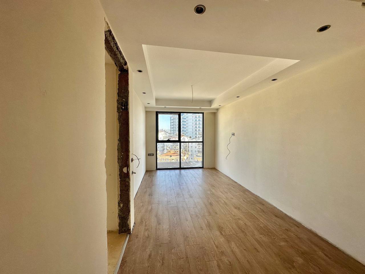 Dar ve boş yatak odası, Tosmur’daki penthouse dairede panoramik pencere ve tamamlanmamış kapı açıklığıyla görülüyor