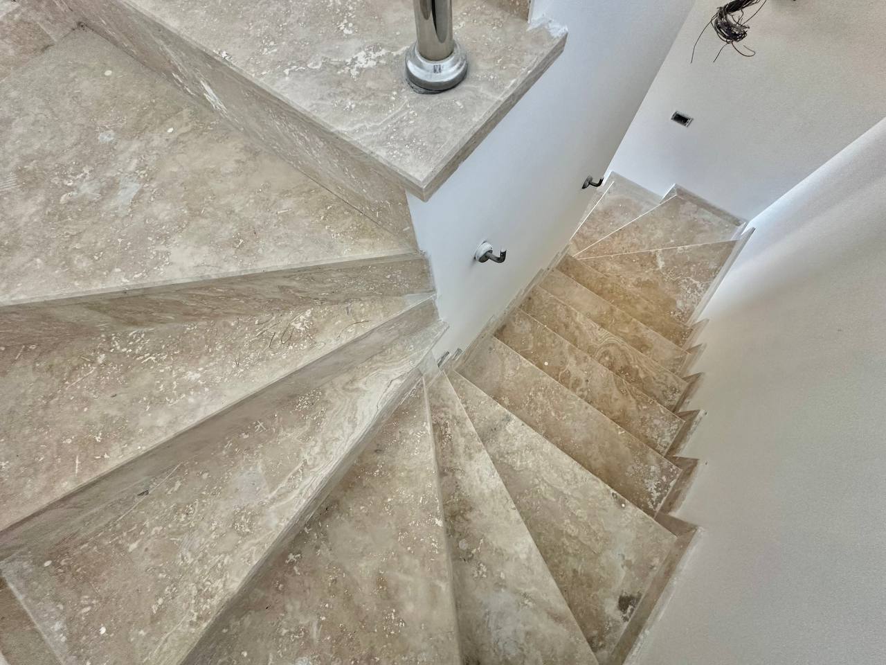 Bej taş basamaklı spiral merdiven, dubleks içinde metal korkuluk ve gömme tavan ışıklarıyla uzanıyor