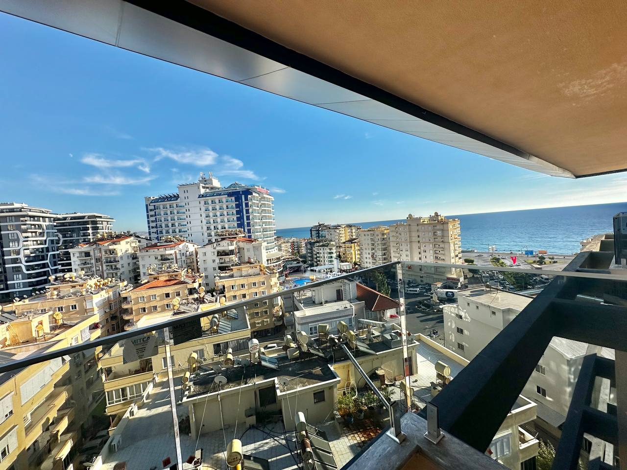 Cam korkuluklu teras, Tosmur’daki satılık penthouse önünde avludaki yuvarlak havuz ve denizle birlikte görülüyor