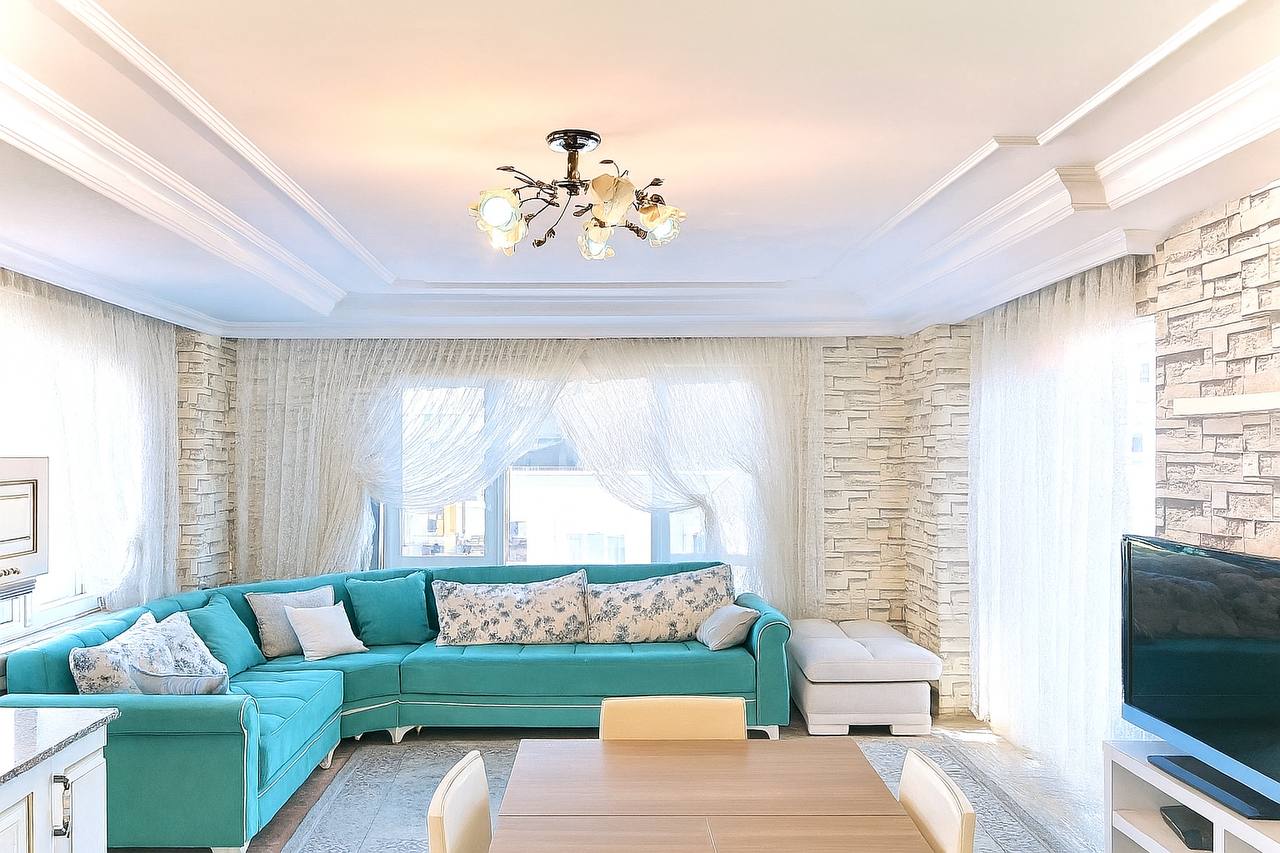 Living room with a turquoise corner sofa and panoramic windows in a penthouse in Tosmur for sale