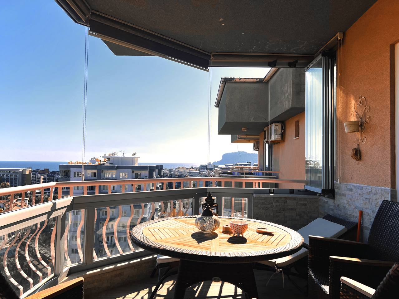 Balcony with corner glazing, wicker chairs and a city view in a penthouse in Tosmur, Turkey
