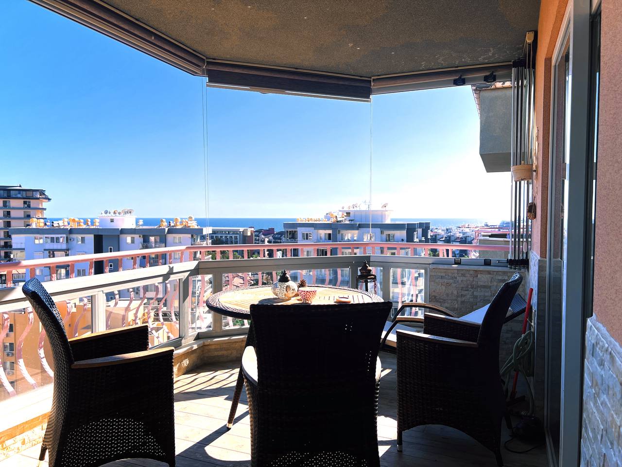 Corner-glazed balcony with wicker chairs overlooking the sea and city