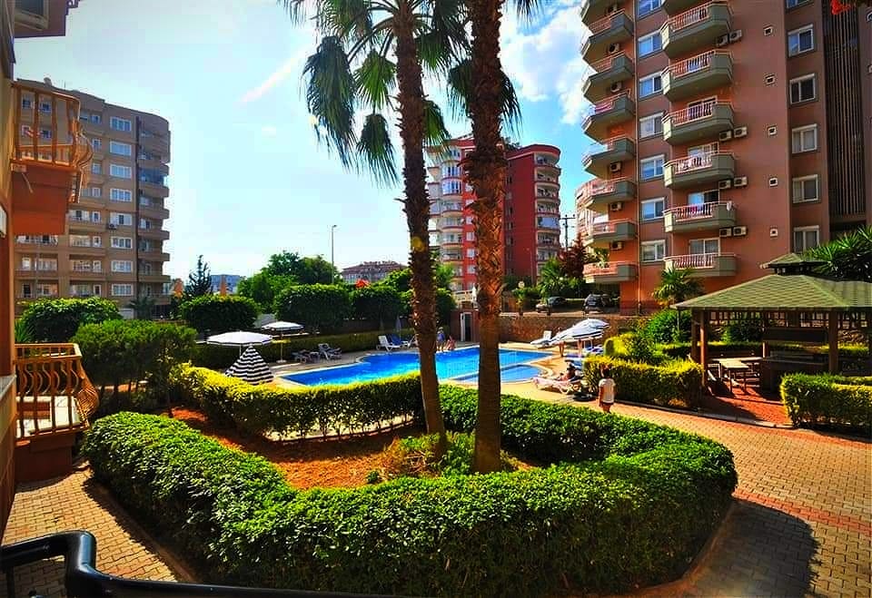 Irregular outdoor pool with palms and a green-roofed gazebo in a complex with apartments in Tosmur, Turkey