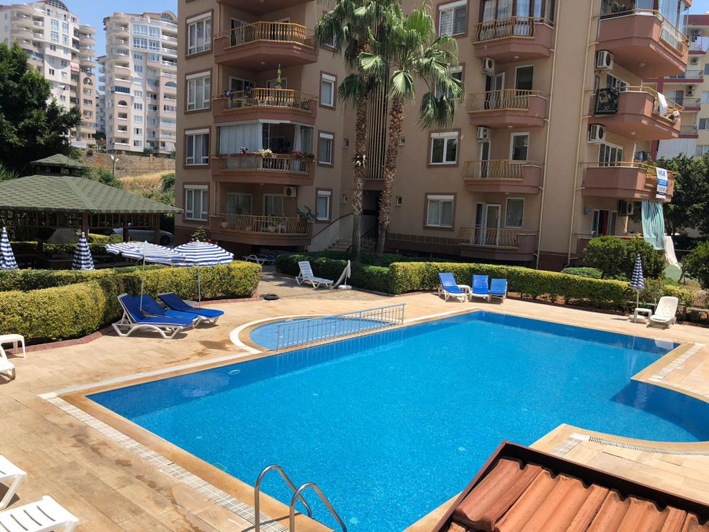 Curved-edge pool with a green gazebo and palms for residents of apartments in Turkey
