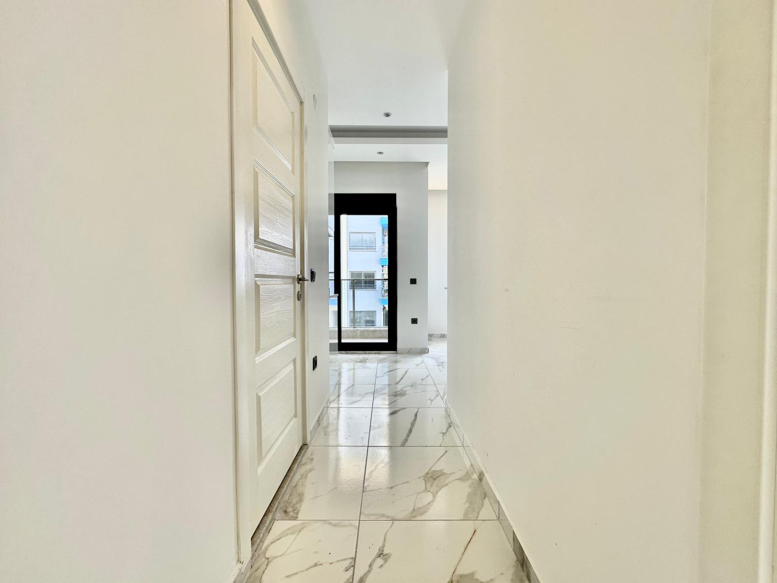 Rezidansın uzun koridorunda beyaz iç kapı ve balkon kapısındaki siyah çerçeve
