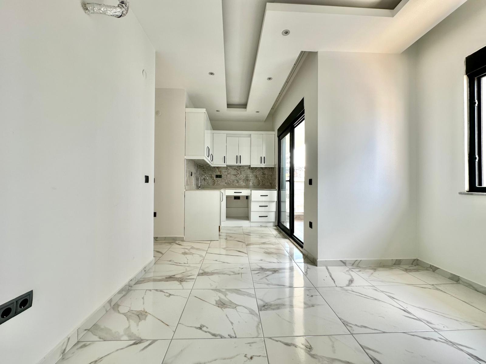 Denize yakın konutun mutfaklı salonunda beyaz dolaplar, mermer arkalık ve siyah balkon kapısı